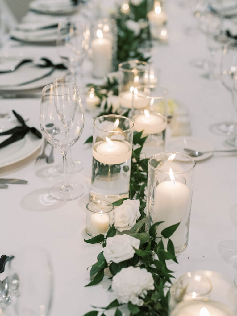 Long reception table decor of pillar candles, floating candles, and greenery with roses down the center.
