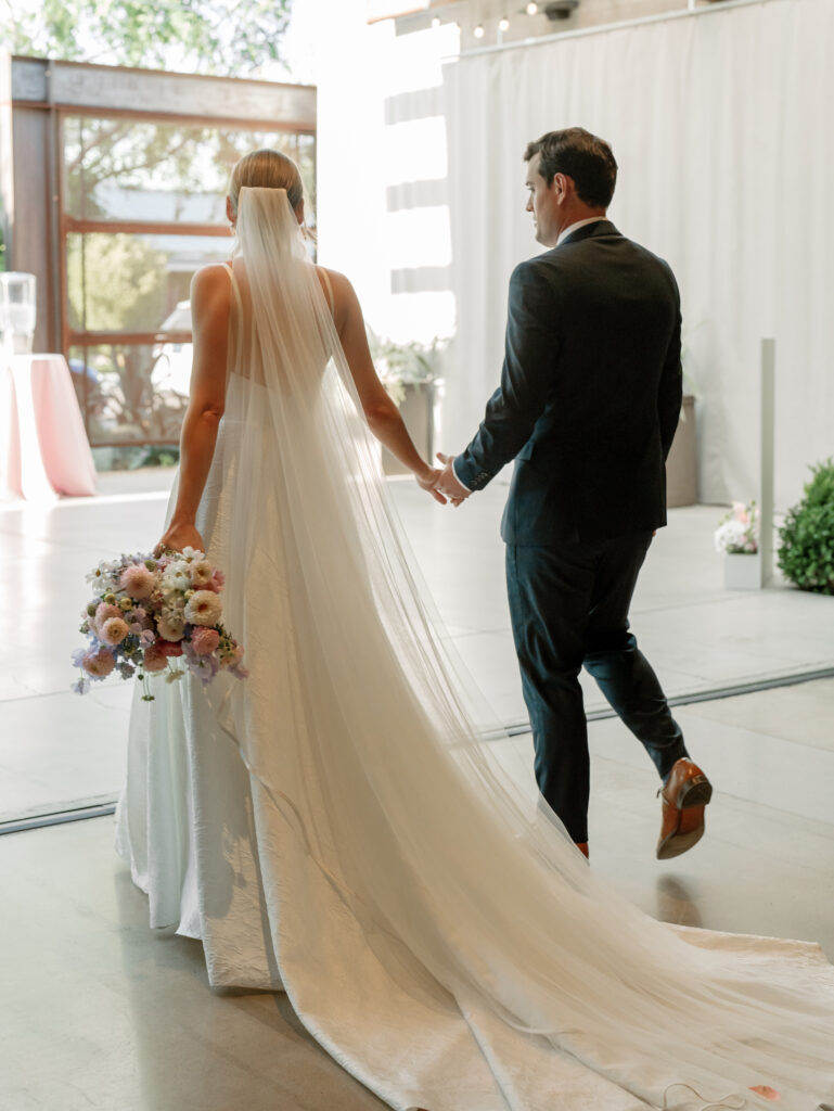 Bride and groom walking away., holding hands and bride holding bouquet.