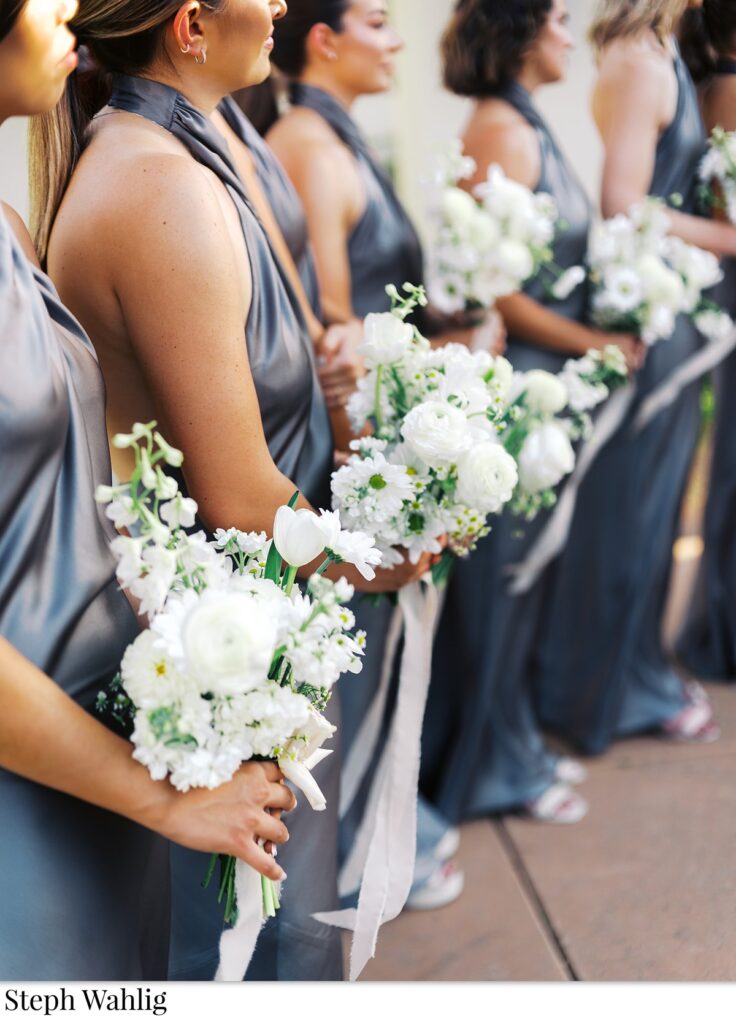 Bridesmaids in blue dresses holding white flowers bouquets.