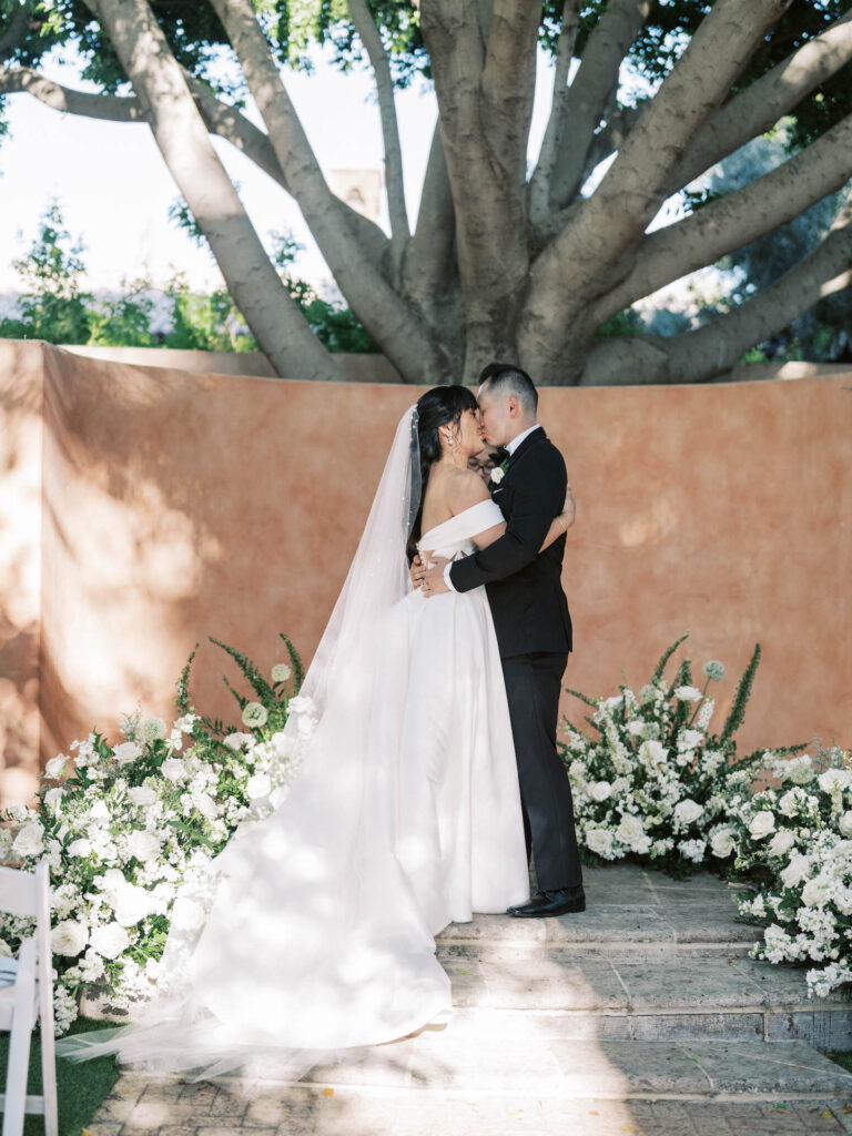 Bride and groom kissing in altar space at Royal Palms with ground floral designs surrounding them of white flowers and greenery.