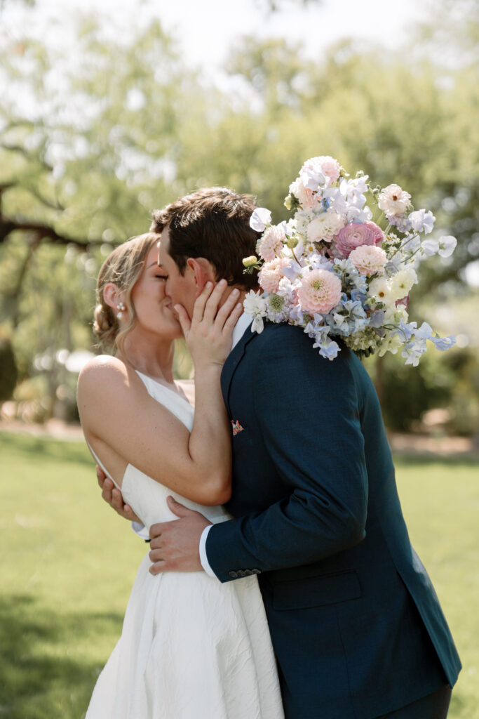 Bride and groom kissing and embracing with groom's arms around bride and bride holding bouquet behind groom.