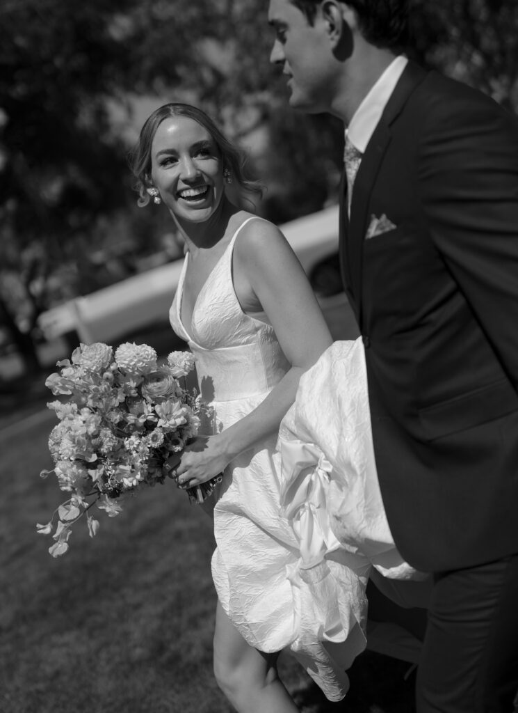 Bride smiling at groom, both walking outside.
