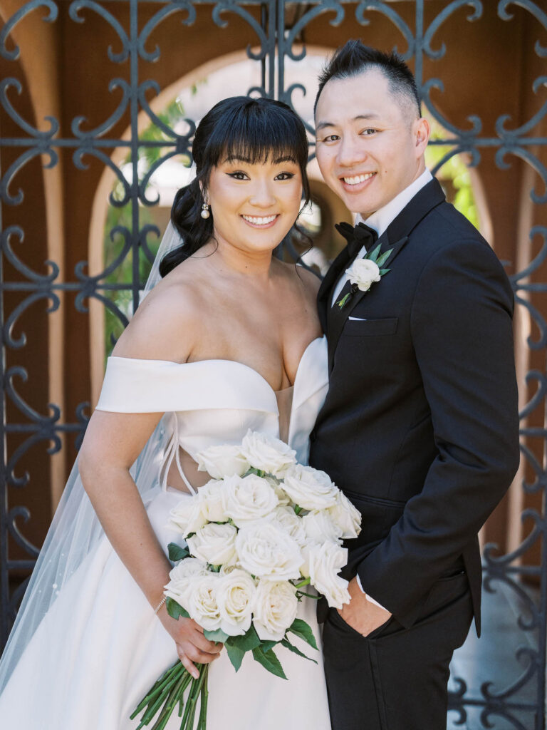 Bride and groom smiling, standing together in front of metal design gate.