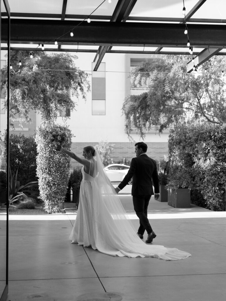 Bride and groom walking away in image, with bride raising bouquet in celebration.