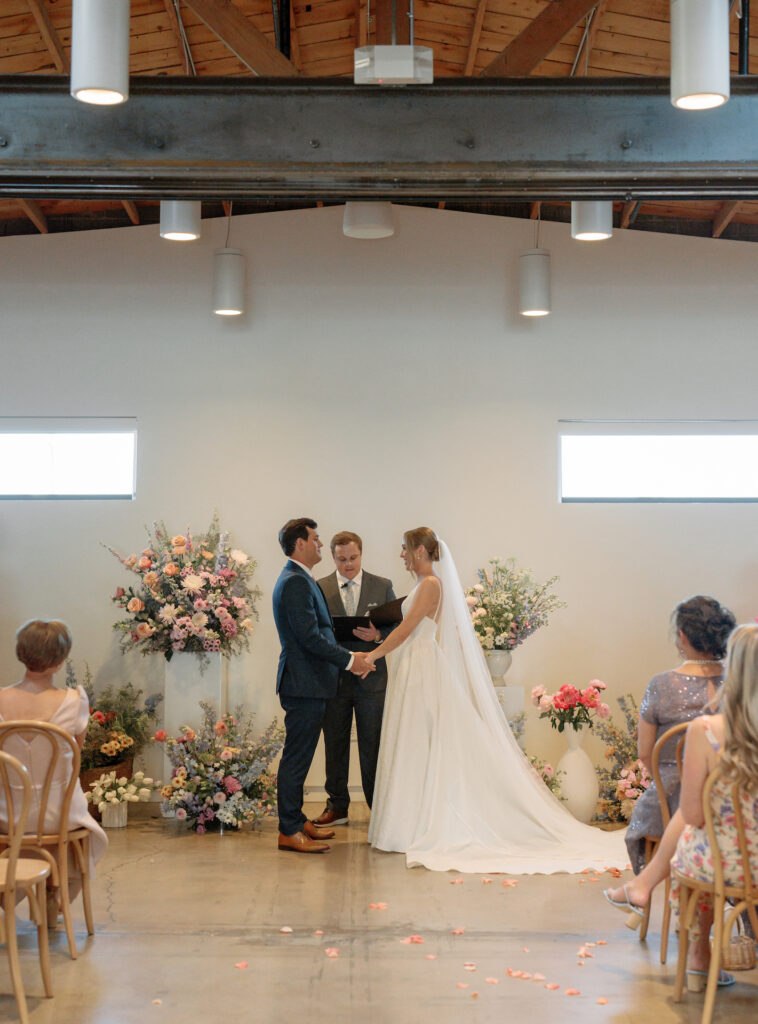 Bride and groom in wedding ceremony altar space with officiant at The Clayton House with floral arrangements around them.