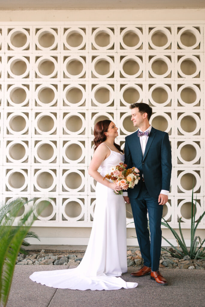 Bride and groom standing in front of pattern design wall at Mountain Shadows, looking at each other and smiling.