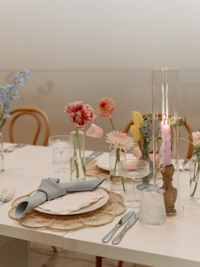 Wedding reception table place setting with pink ribbed taper candles and bud vases of floral.
