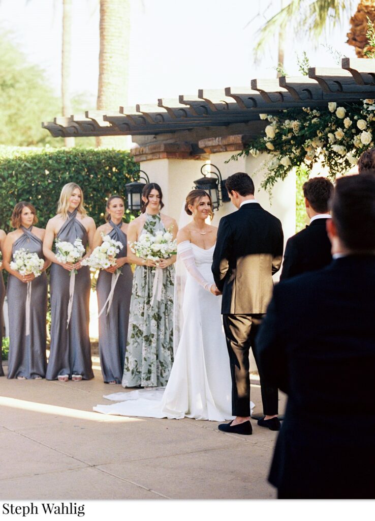 Bride and groom holding hands in wedding ceremony altar space with bridesmaids and groomsmen on either side in a line.