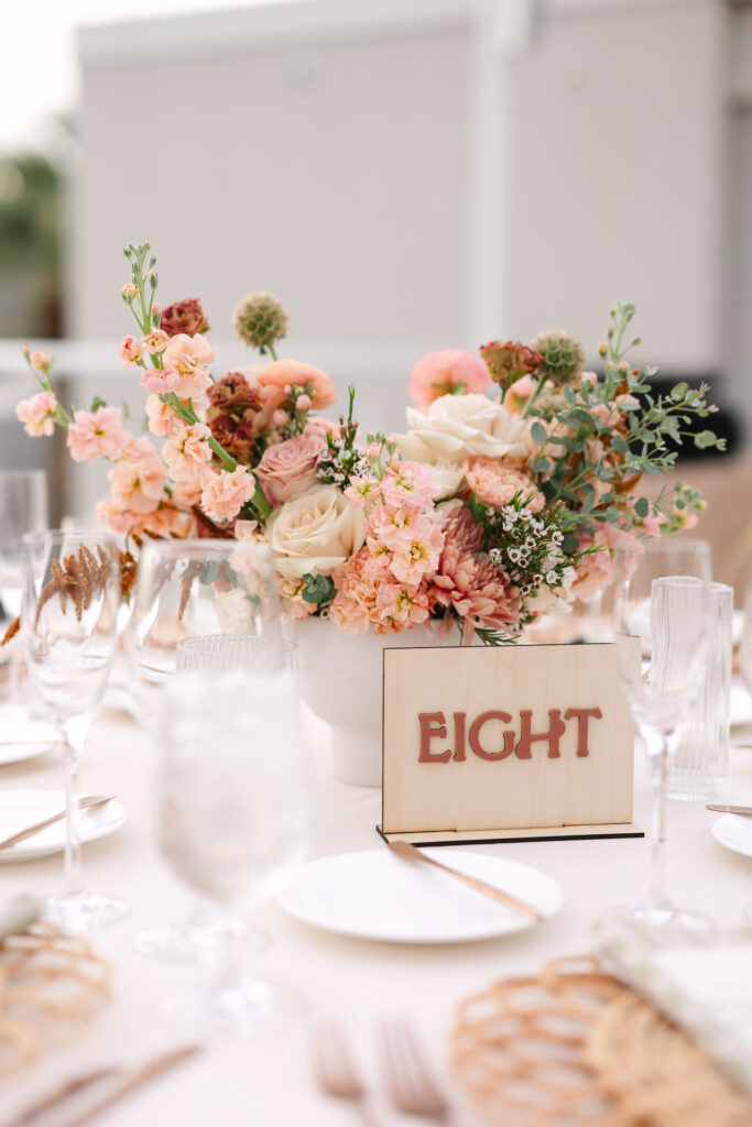Wedding reception table design with centerpiece of flowers with a wooden table number sign.