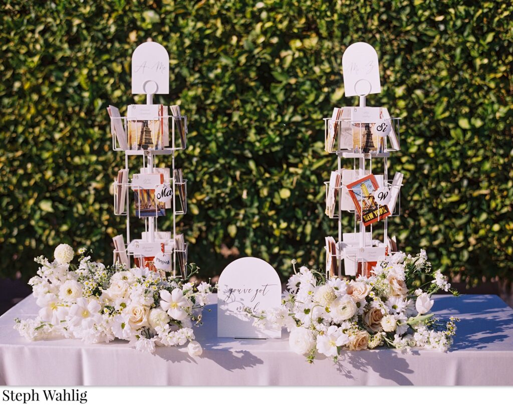 Wedding guest escort cards in post card holders on a table with white flowers.