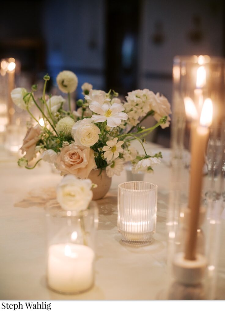 Wedding reception small floral centerpiece with votive candles and taper candles by it.