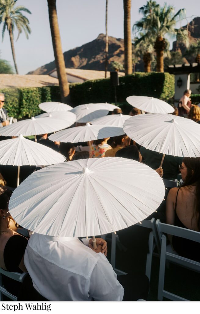 Guests holding white umbrellas opened above them at wedding ceremony.