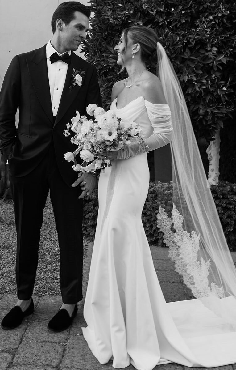 Bride and groom smiling at each other in front of desert landscape, bride holding bouquet.