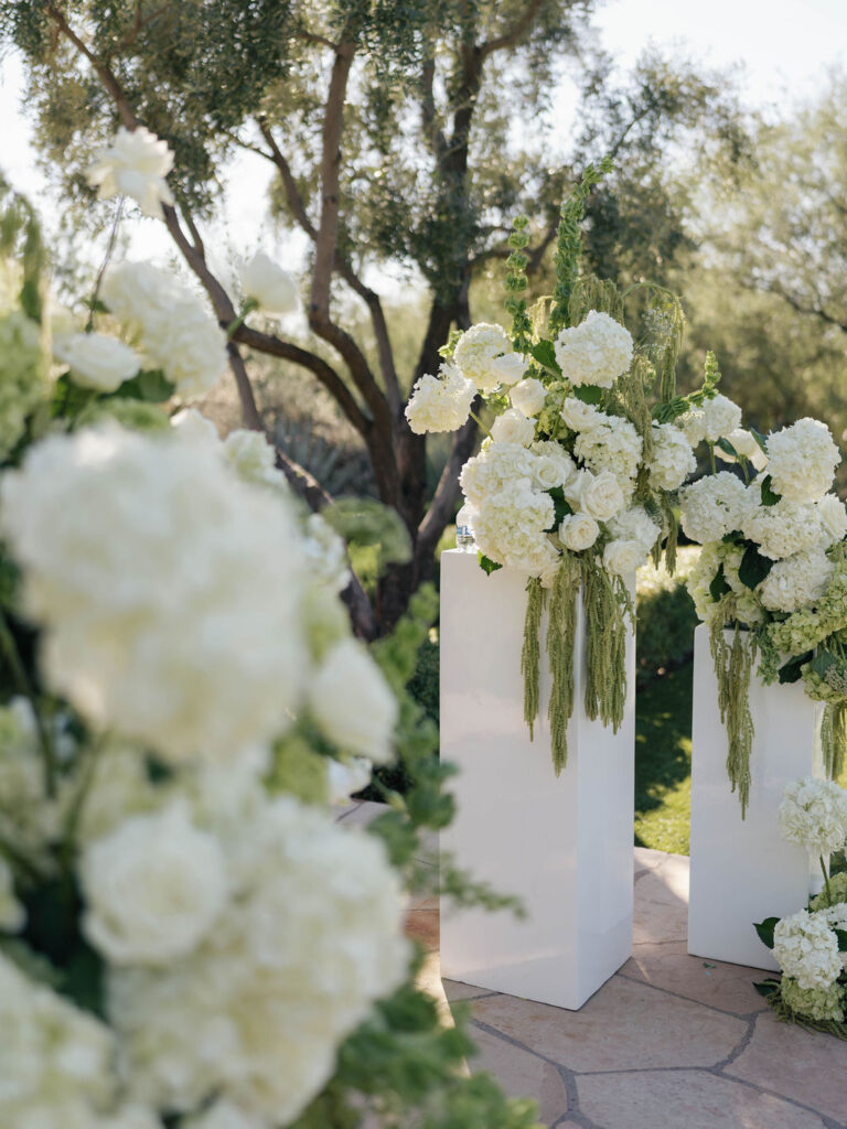 Wedding ceremony altar space floral design on white acrylic columns with white roses and white and green hydrangeas and green amaranthus.