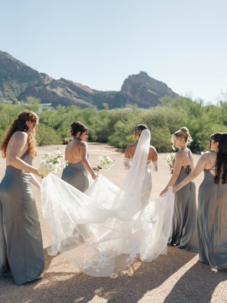 Bride walking away with bridesmaids holding her veil.