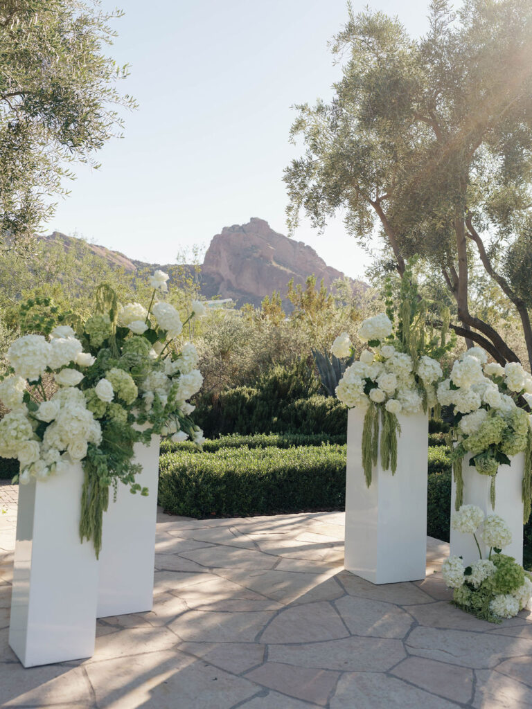 Wedding ceremony altar space floral design on white acrylic columns with white roses and white and green hydrangeas and green amaranthus.