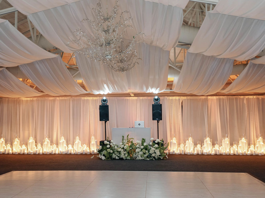 Indoor dance floor surrounded by candles and drapery with floral in front of the DJ table.