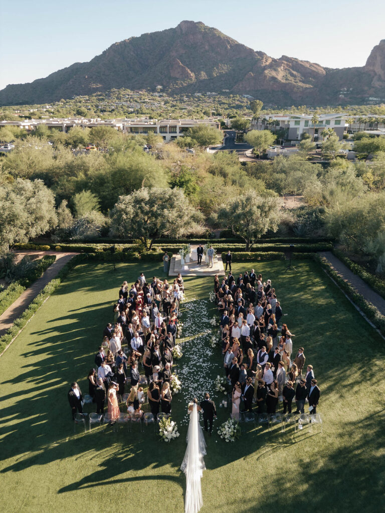 Overhead view of El Chorro outdoor wedding ceremony with Camelback Mountain in the distance. Guests are standing facing the bride entering the aisle.