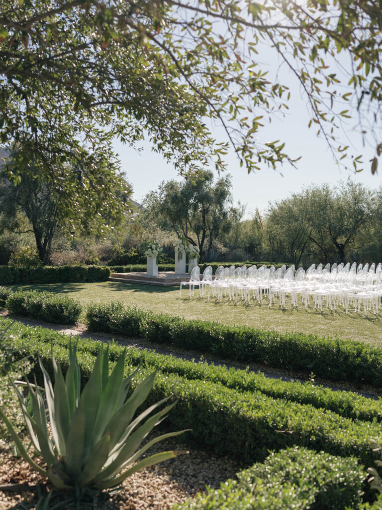 Wedding ceremony altar space floral design on white acrylic columns with white roses and white and green hydrangeas and green amaranthus. Clear acrylic guest chairs.