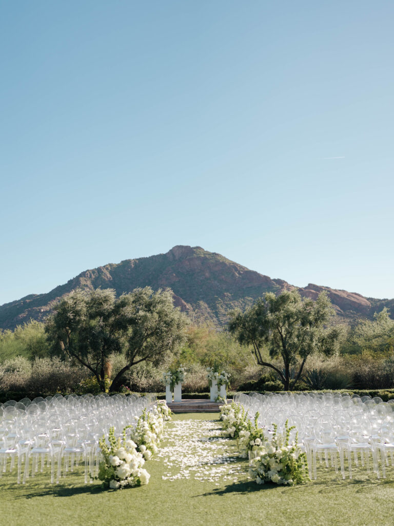 Wedding ceremony altar space floral design on white acrylic columns with white roses and white and green hydrangeas and green amaranthus. Clear acrylic guest chairs.
