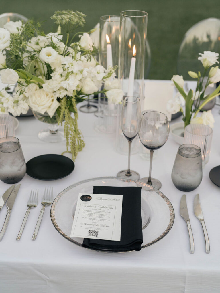 Wedding reception table design of black and white place settings, candles, and white and green floral centerpieces.