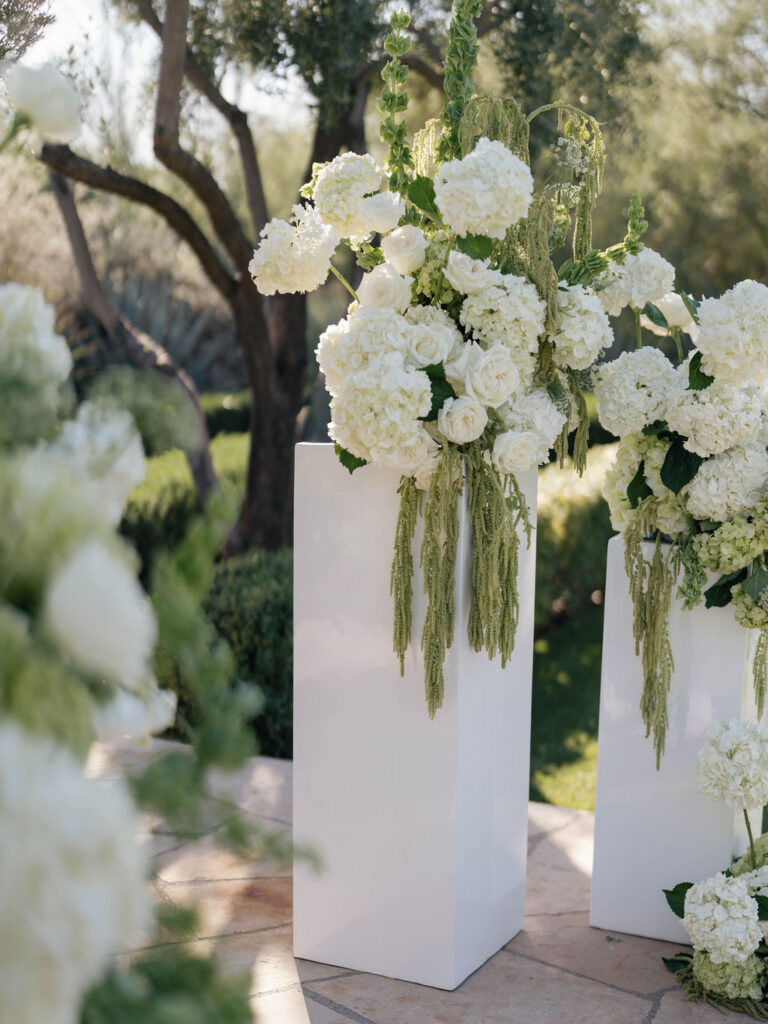 Wedding ceremony altar space floral design on white acrylic columns with white roses and white and green hydrangeas and green amaranthus.