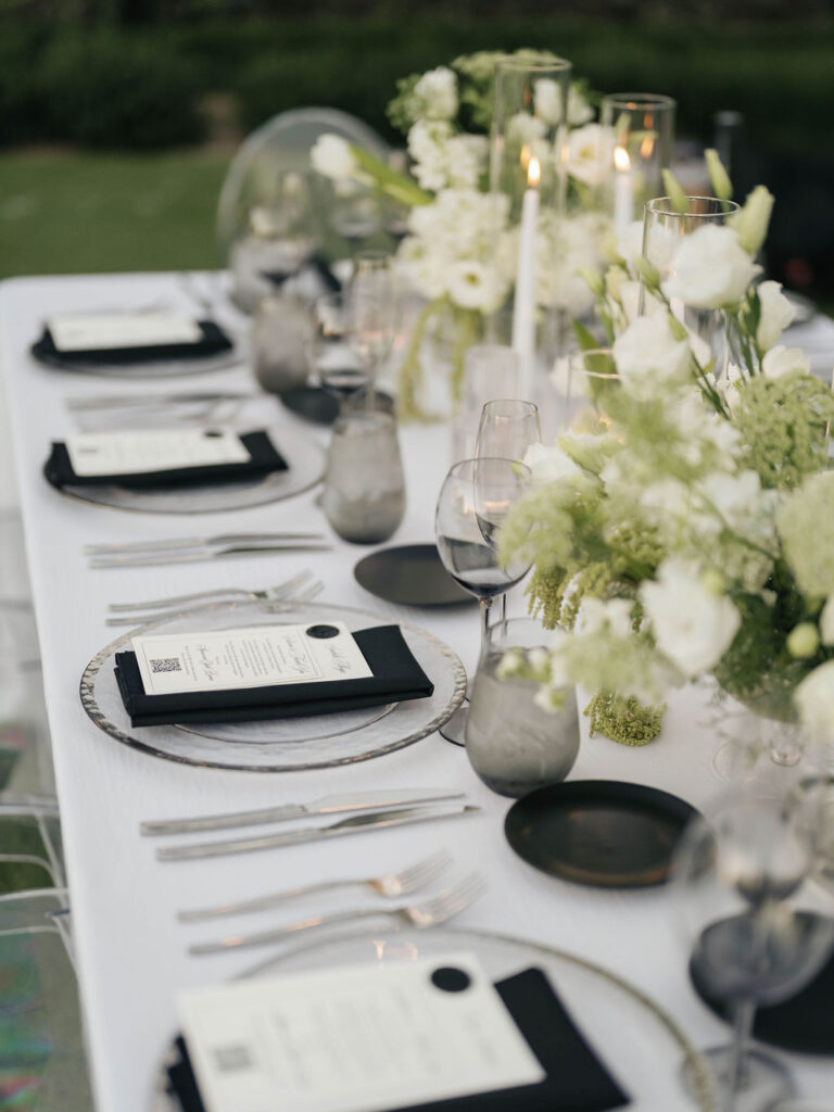 Wedding reception table design of black and white place settings, candles, and white and green floral centerpieces.