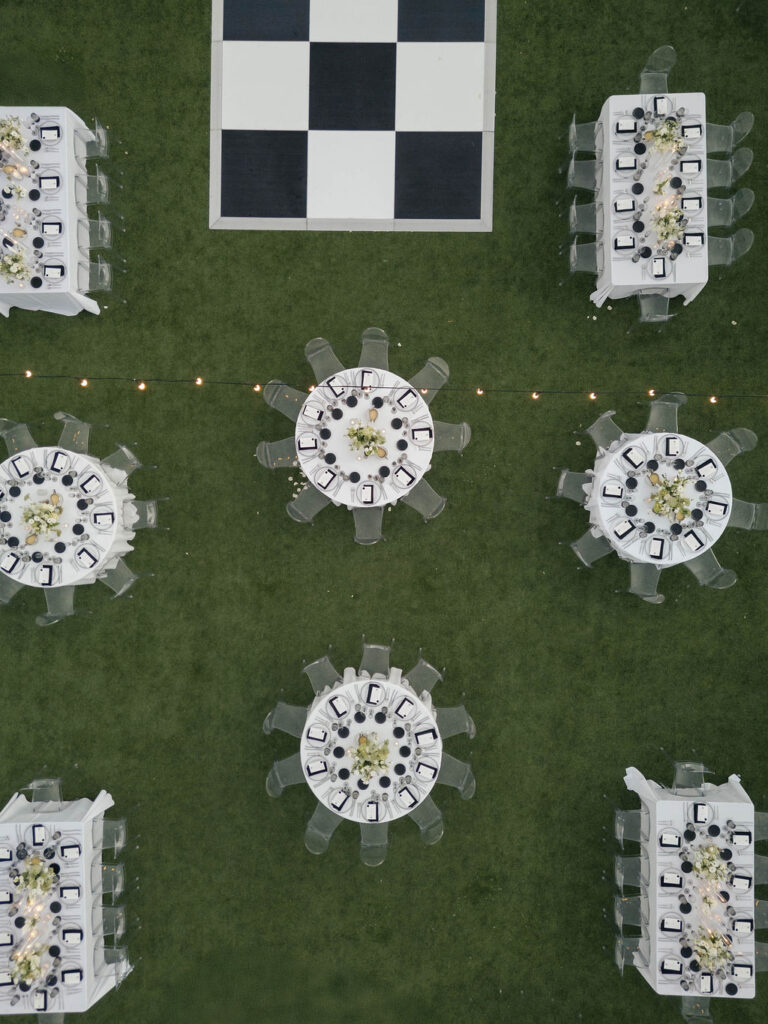 Overhead image of wedding reception with black and white checkered dance floor and round and rectangle guest tables with white tablecloths, flowers and black and white place settings.