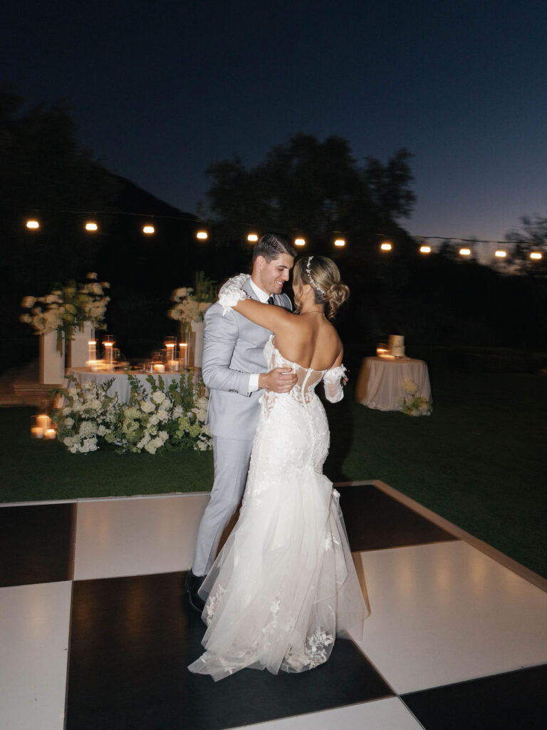 Bride and groom dancing outside in the evening on black and white checkered dance floor.