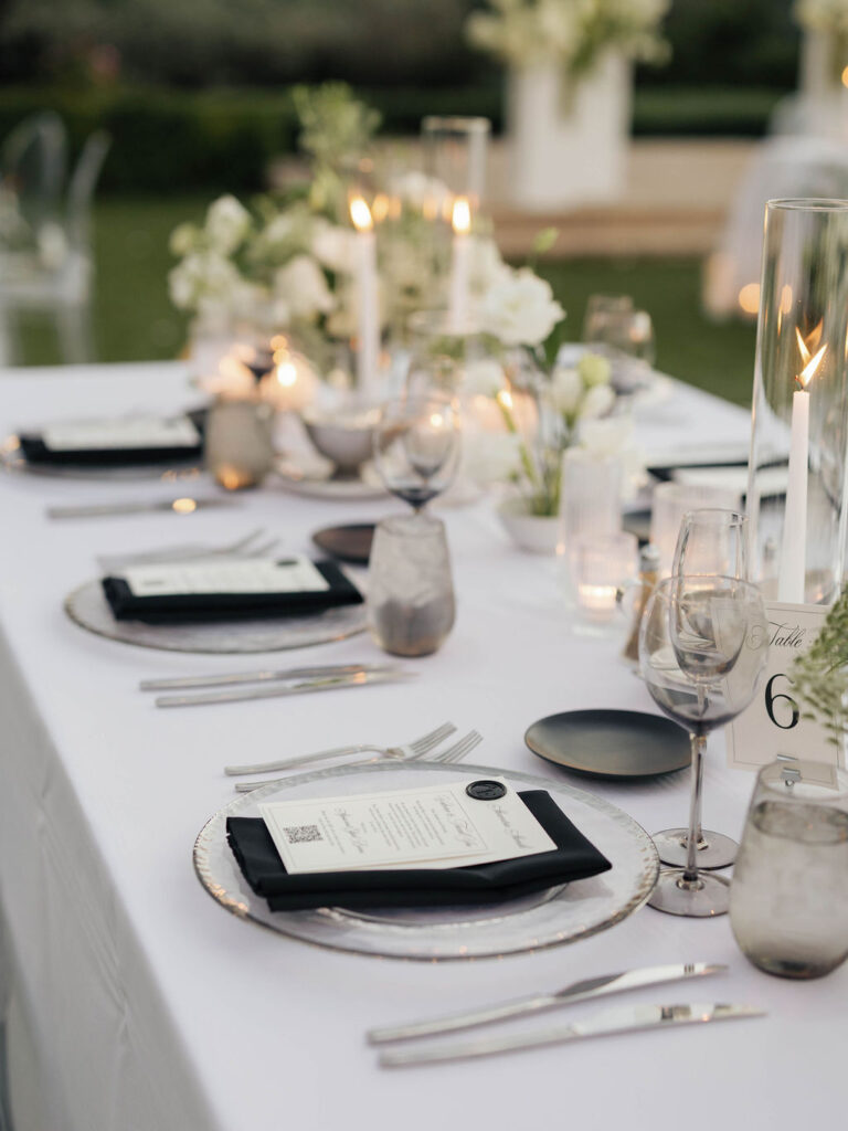 Wedding reception table design of black and white place settings, candles, and white and green floral centerpieces.