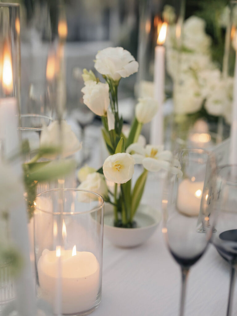 White lisianthus flowers in small bowl with flower frog as centerpiece. Surrounded by candles and place setting element.