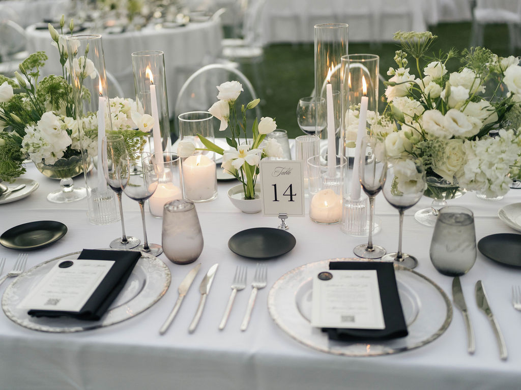 Wedding reception table design of black and white place settings, candles, and white and green floral centerpieces.