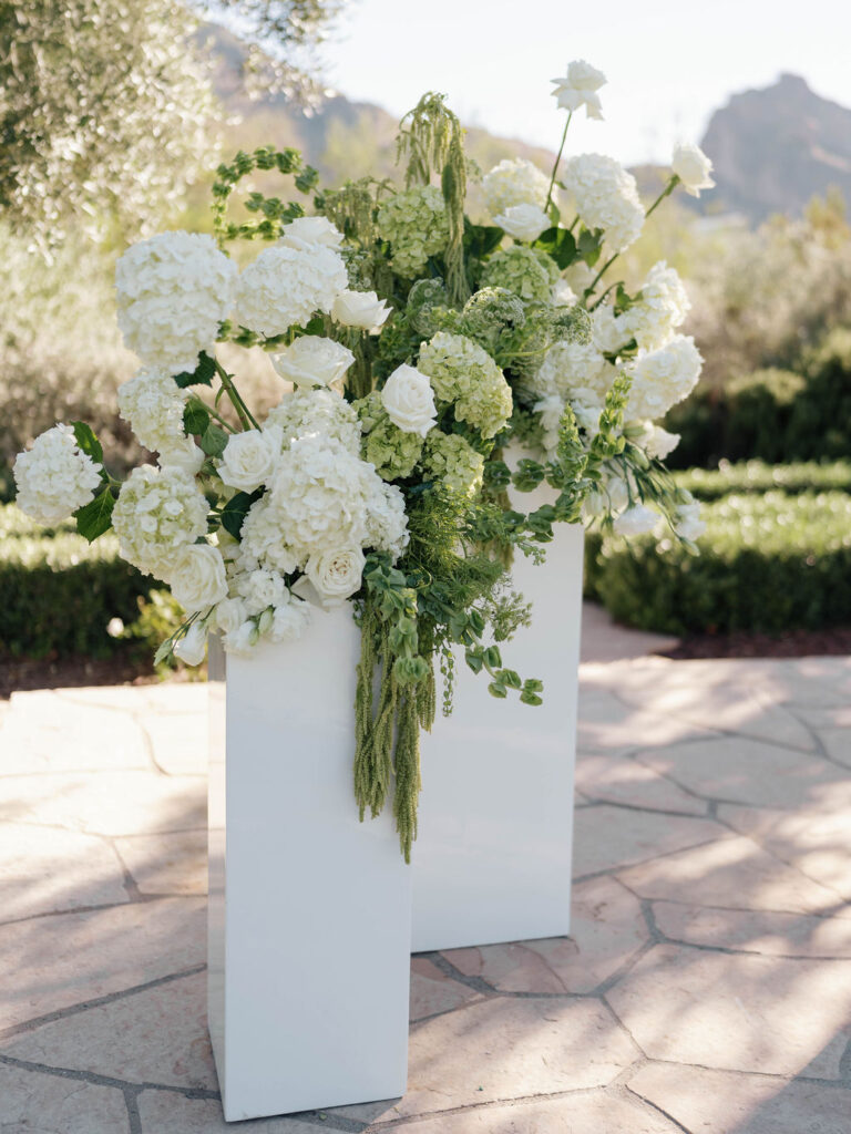 Wedding ceremony altar space floral design on white acrylic columns with white roses and white and green hydrangeas and green amaranthus.