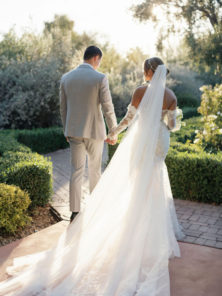 Bride and groom walking away on brick path holding hands.