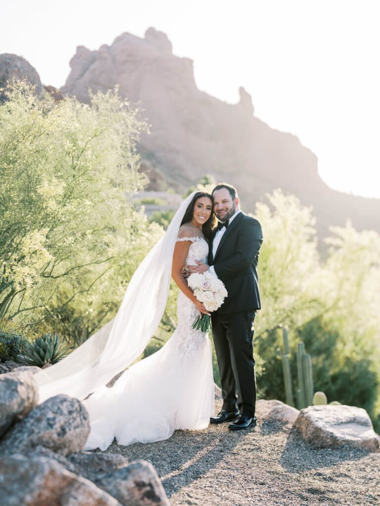 Bride and groom embracing, smiling, standing on desert path.