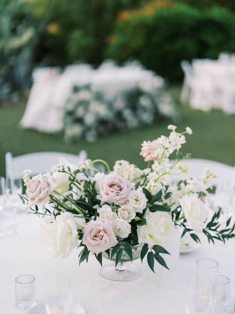 Low wedding reception centerpiece of white and blush flowers with greenery.
