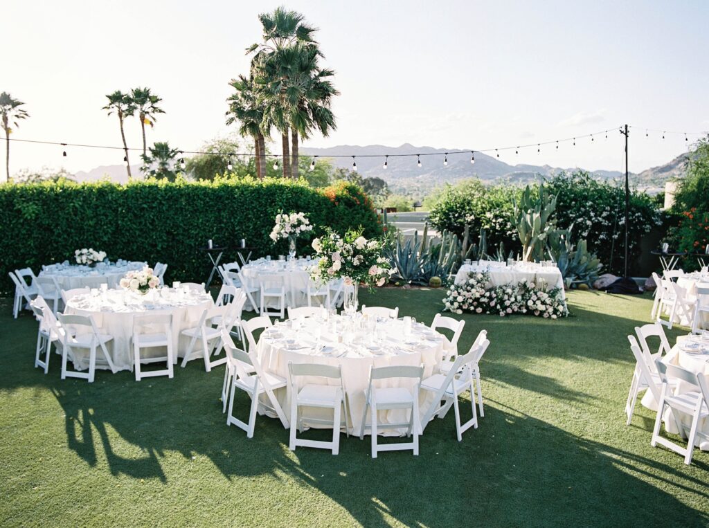 Outdoor wedding reception with tall round table centerpieces of white and blush flowers and greenery.