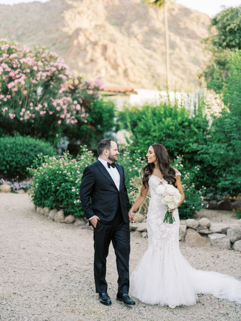 Bride and groom smiling, holding hands and walking on desert path.