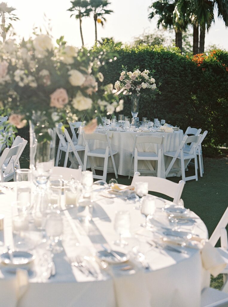 Outdoor wedding reception with tall round table centerpieces of white and blush flowers and greenery.