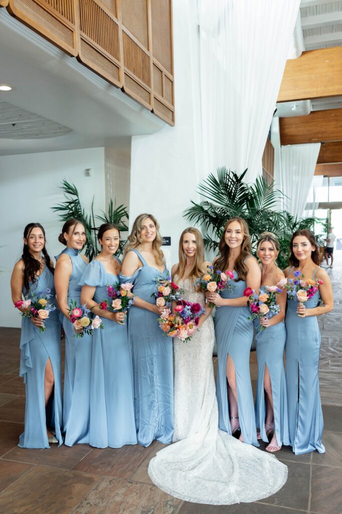 Bride standing in a line with bridesmaids wearing light blue dresses. All holding bouquets.