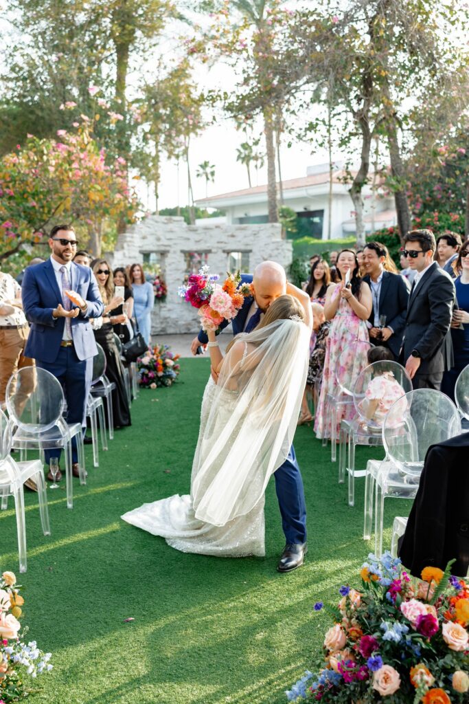 Bride and groom kissing in wedding ceremony aisle with groom dipping bride.