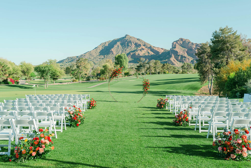 Outdoor wedding ceremony gold circle arch in front altar space with two asymmetrical floral arrangements installed on it. Mountains in background.