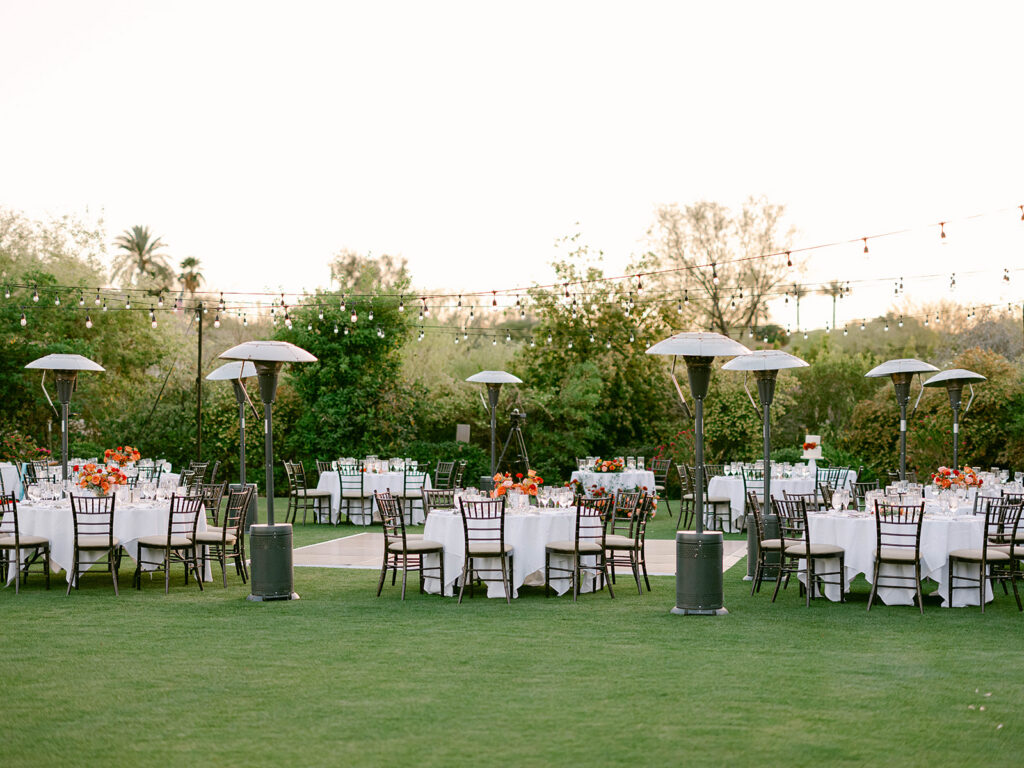 Outdoor wedding reception space at Paradise Valley Country Club with round guest tables, dance floor in center and heat lamps placed around.