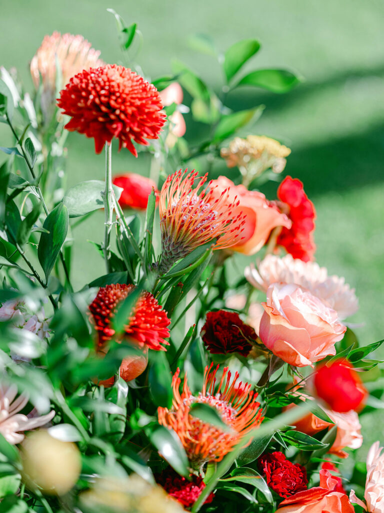 Wedding flowers in pink, peach, orange, and red with greenery in an arragement.