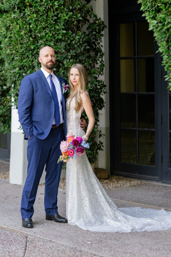 Bride and groom standing next to each other, looking at camera, bride holding bouquet.