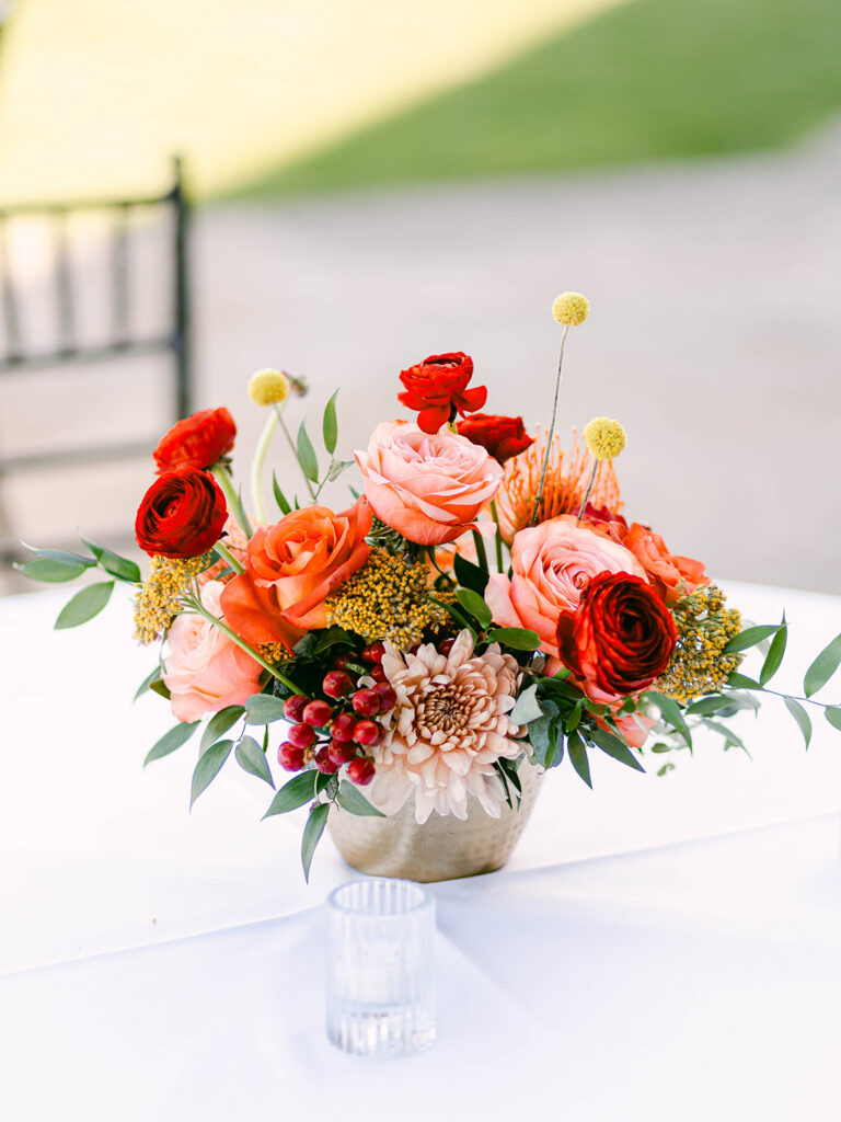 Wedding reception centerpiece in gold vase of pink, peach, orange, and red flowers.