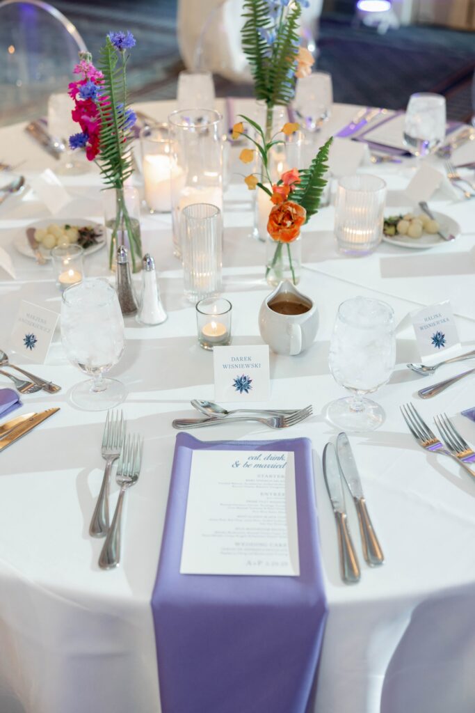 Wedding reception place setting with bud vase floral in center of table with pillar and votive candles.